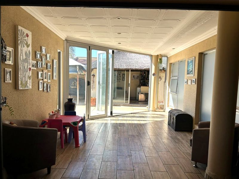 A spacious enclosed patio featuring wood-look tiled flooring, a decorative coffered ceiling, and large bi-fold glass doors opening to the rear garden area.
