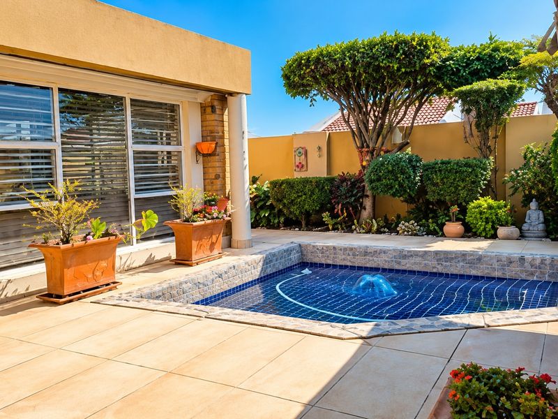 A well-maintained outdoor pool area featuring a tiled patio, built-in swimming pool, and landscaped garden with boundary walls.