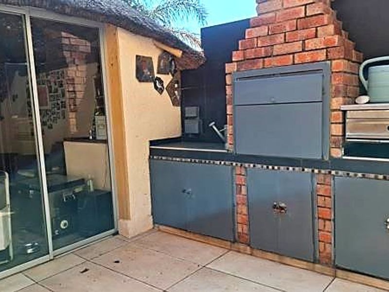 Covered outdoor patio area featuring a built-in brick braai, tiled flooring, and sliding door access to the interior living space.