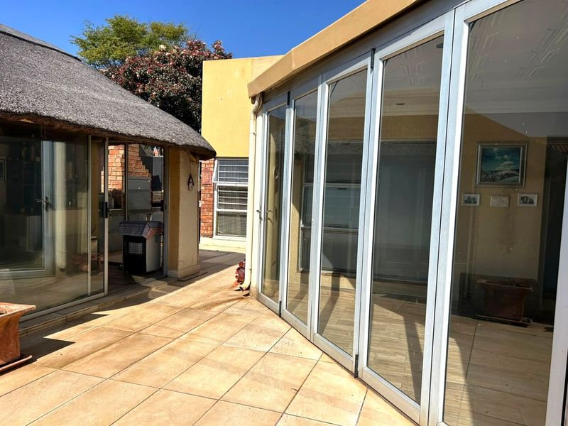 A spacious outdoor patio area featuring tiled flooring, aluminium stacker doors, and a covered thatch roof section, ideal for outdoor entertaining.