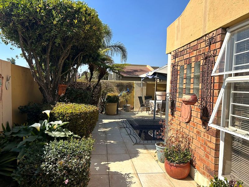 A private rear courtyard featuring a paved patio area, established garden landscaping, and a brick exterior wall with decorative accents.