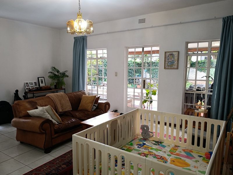 A bright living room featuring tiled flooring, large multi-pane windows, and french doors providing direct access to the outdoor patio area.