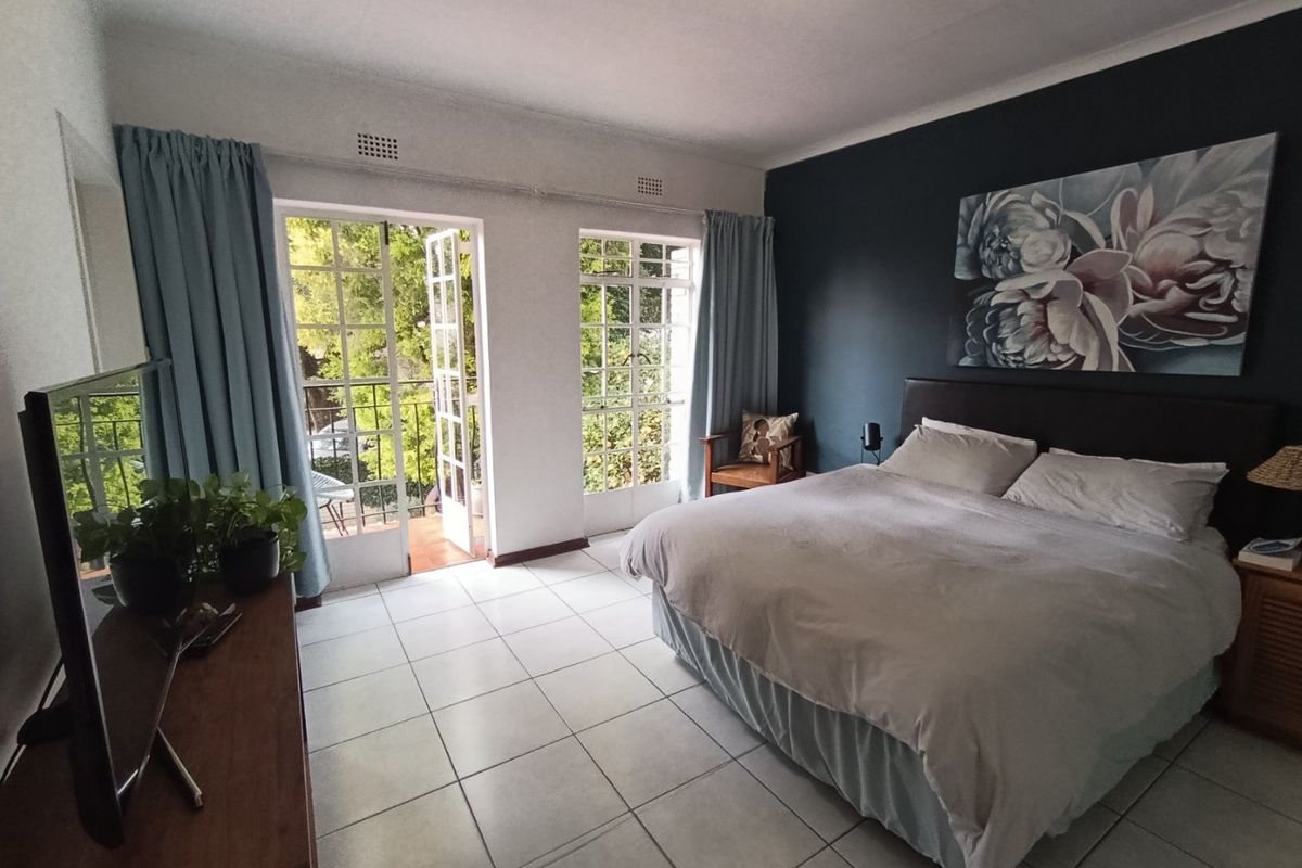 Spacious bedroom featuring tiled flooring, a dark accent wall, and double french doors providing direct access to a private balcony.