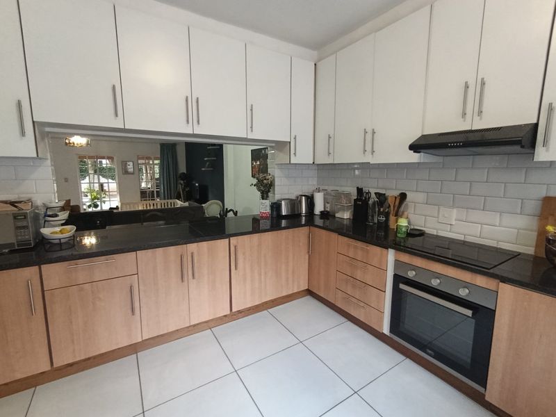 Modern kitchen featuring white upper cabinets, wood-finish lower cabinetry, granite countertops, subway tile backsplash, and integrated stainless steel oven and hob.