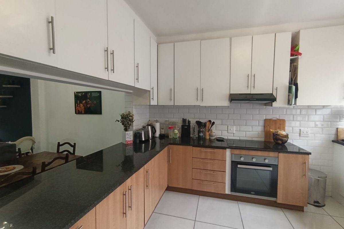 A functional kitchen featuring granite countertops, subway tile backsplash, built-in oven, electric hob, and a mix of white and wood-finish cabinetry.