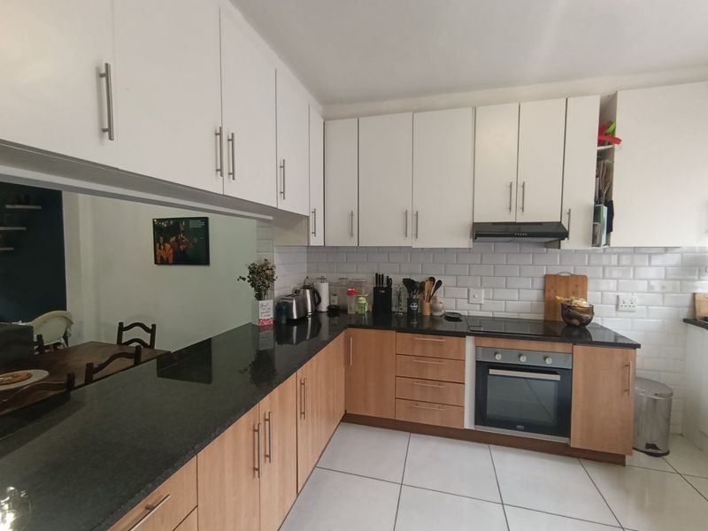 A functional kitchen featuring granite countertops, subway tile backsplash, built-in oven, electric hob, and a mix of white and wood-finish cabinetry.