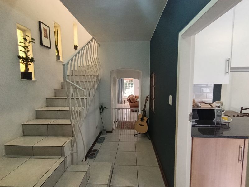 A bright hallway featuring a tiled staircase with a decorative wrought iron balustrade, leading through an archway towards the living area.