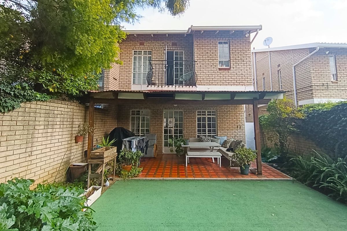 Rear view of the townhouse featuring a covered patio with terracotta tiles, a small balcony, and a private garden area with artificial lawn.