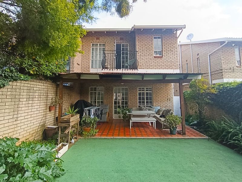 Rear view of the townhouse featuring a covered patio with terracotta tiles, a small balcony, and a private garden area with artificial lawn.