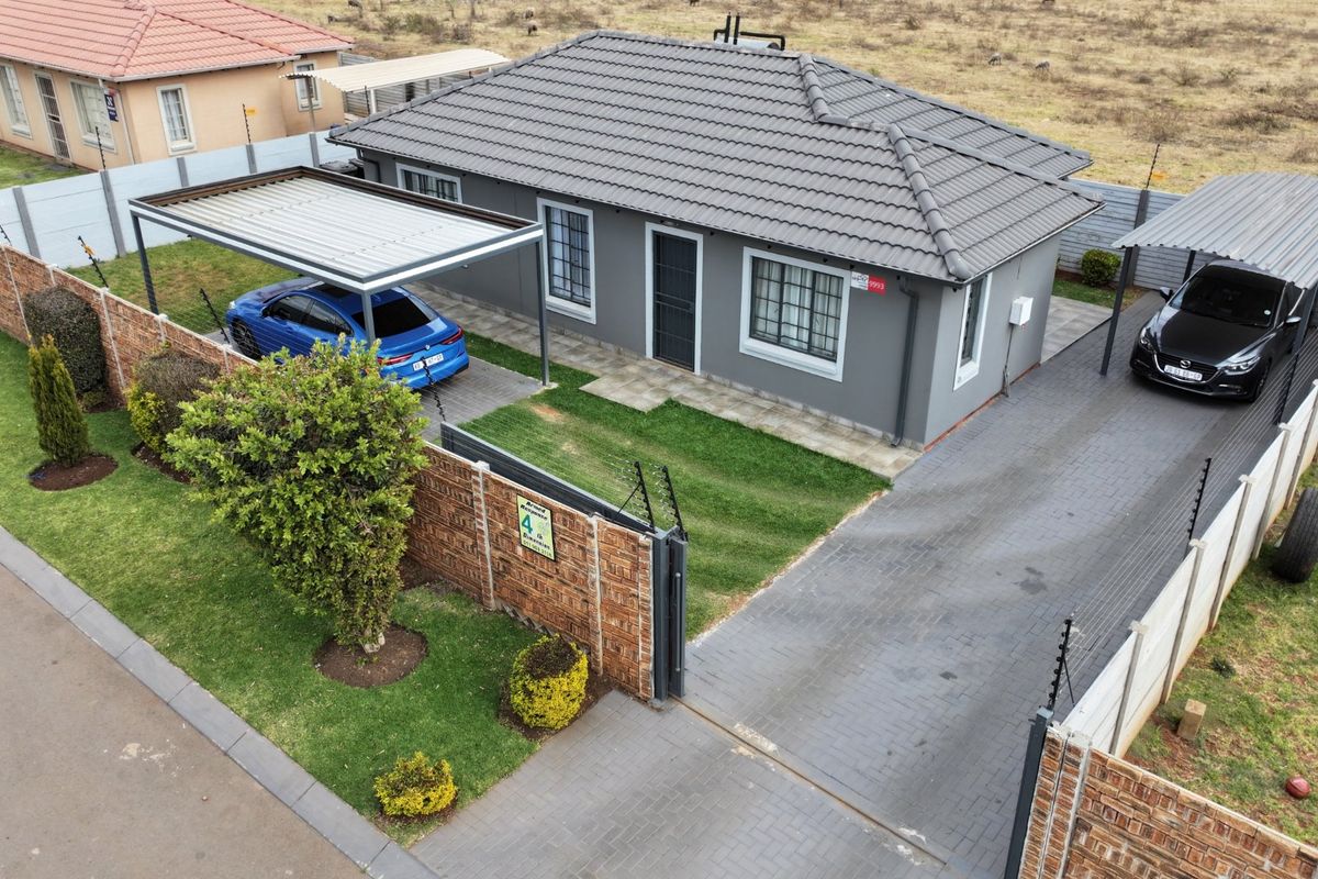 Aerial view of a well-maintained detached house featuring a tiled roof, paved driveway, double carport, and secure perimeter wall with electric fencing.