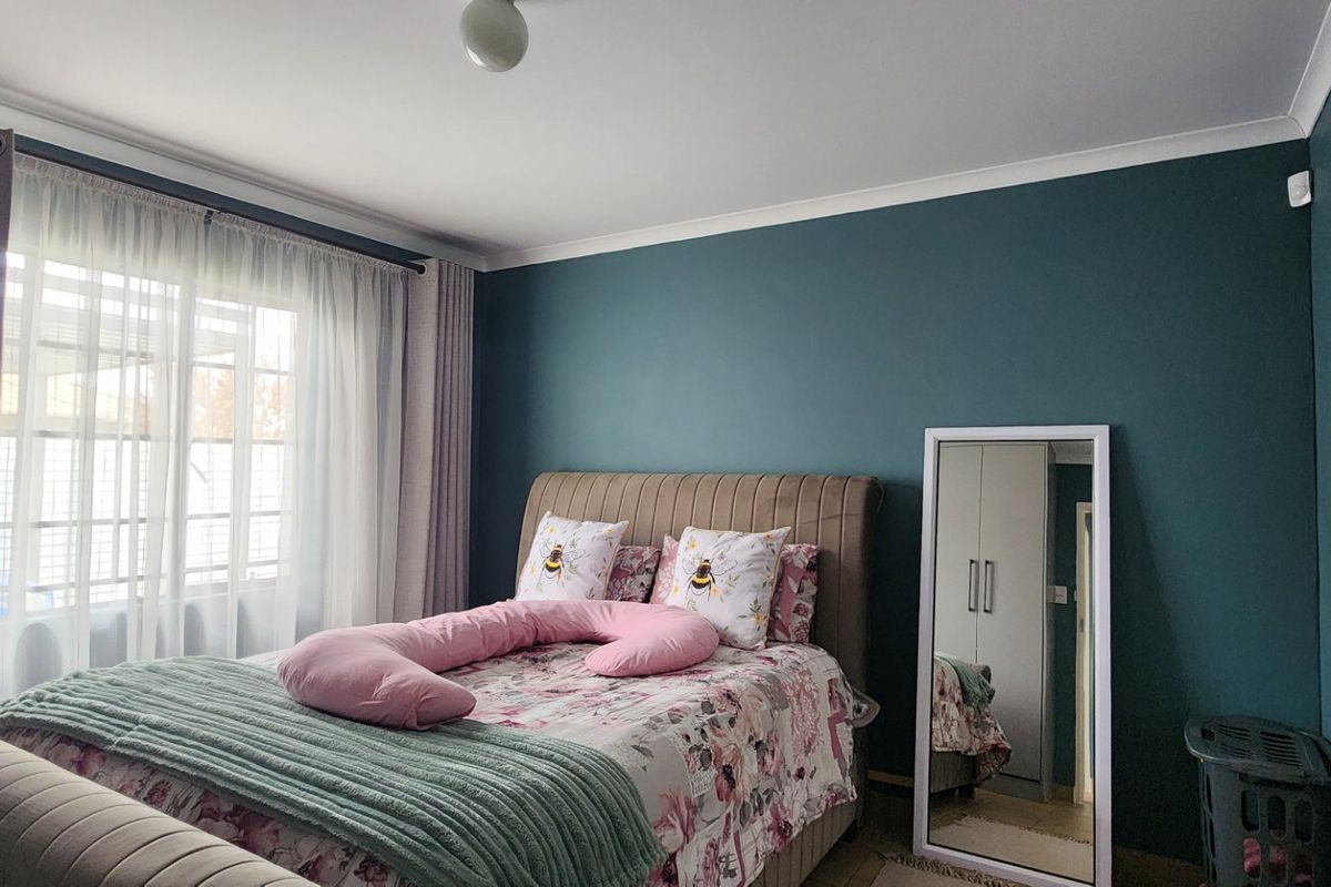 A well-maintained bedroom featuring teal accent walls, built-in cupboards, and large windows allowing for natural light.