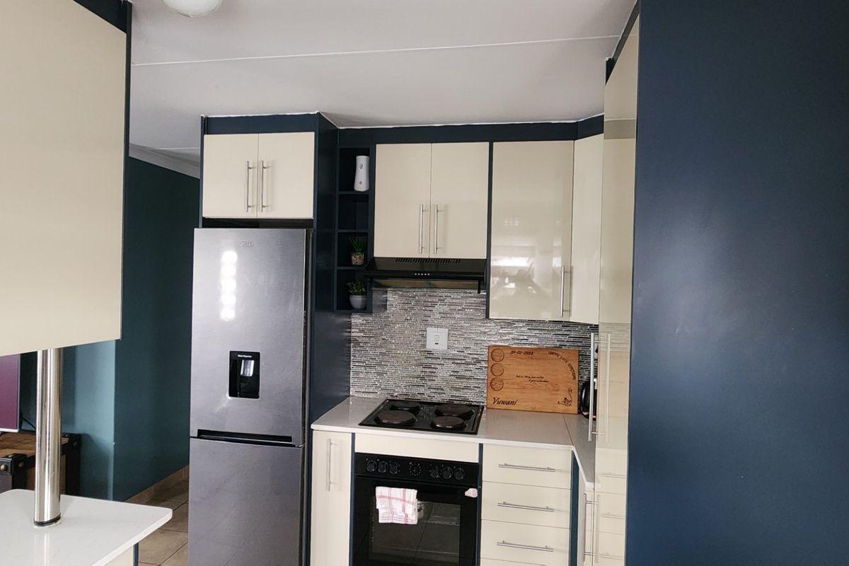A modern kitchen featuring two-tone cabinetry, a tiled backsplash, built-in oven and hob, and a stainless steel refrigerator.