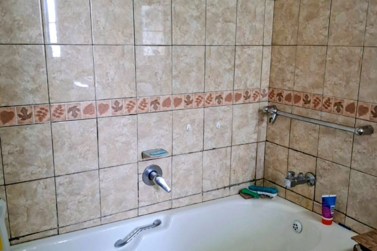 A functional bathroom featuring a built-in bathtub with wall-mounted fixtures and dated ceramic wall tiling.