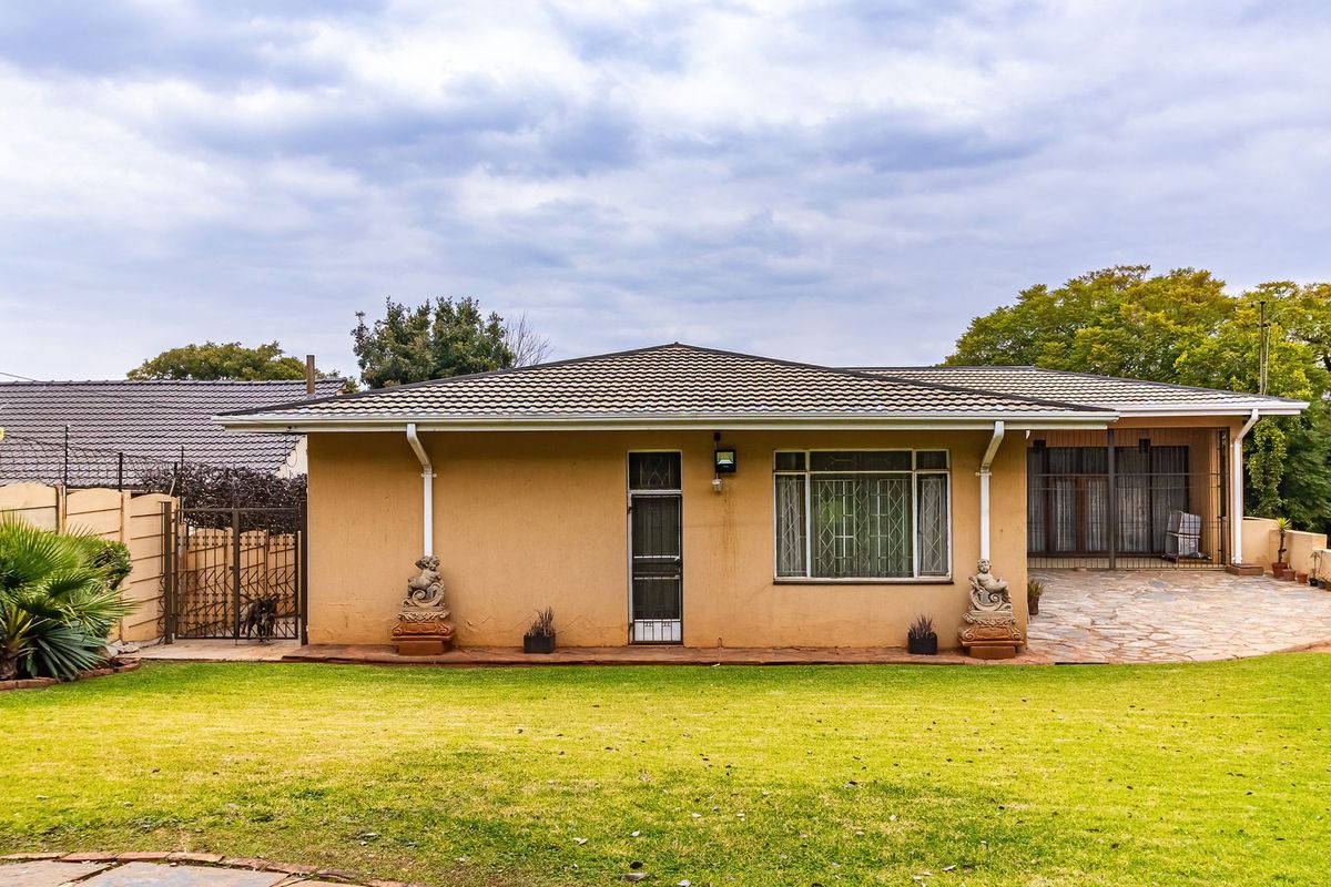 Rear view of the house featuring a tiled roof, stone paved patio area, and a well-maintained lawn with perimeter security walling.