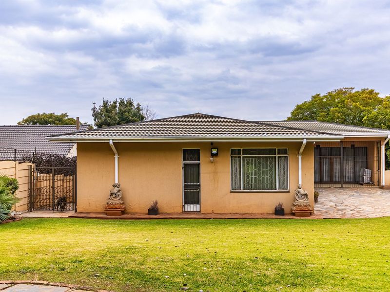 Rear view of the house featuring a tiled roof, stone paved patio area, and a well-maintained lawn with perimeter security walling.