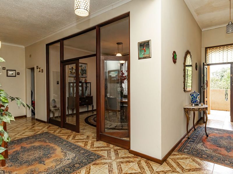 Spacious entrance hall featuring decorative tiled flooring, timber-framed glass partitions, and a solid timber front door leading to the exterior.
