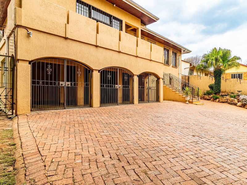 Front exterior view of a multi-level house featuring a large brick-paved driveway, triple garage with security gates, and an external staircase leading to a balcony.