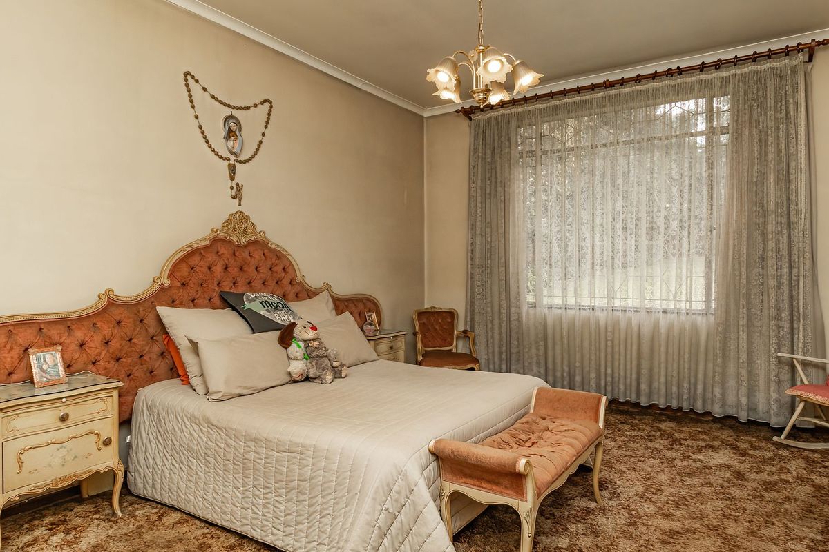 Spacious bedroom featuring classic coving, a central light fixture, and large window with curtain rod, offering a traditional layout ready for modernization.