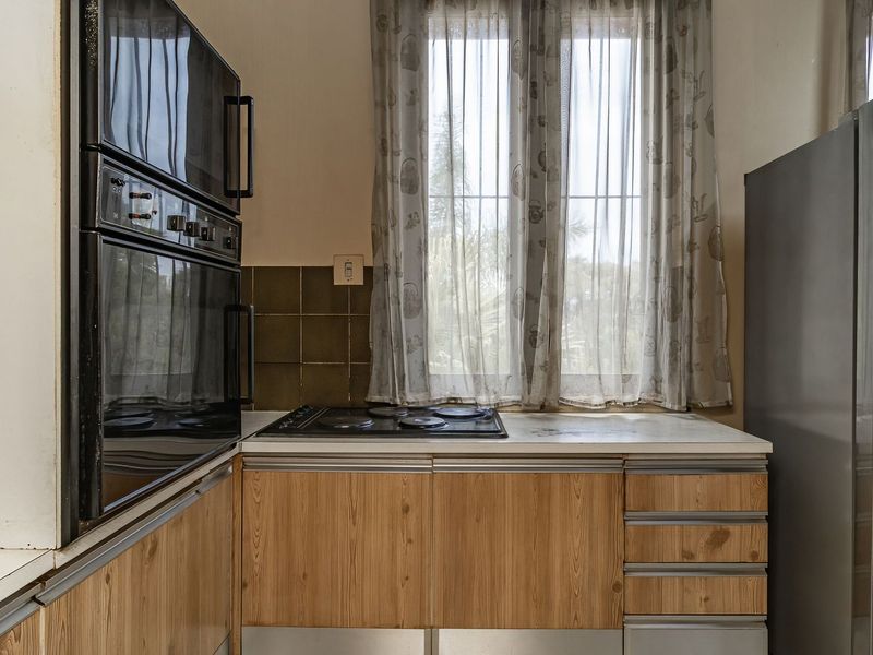 A functional kitchen featuring built-in oven and microwave, electric hob, and wood-look cabinetry with a tiled backsplash and window for natural light.