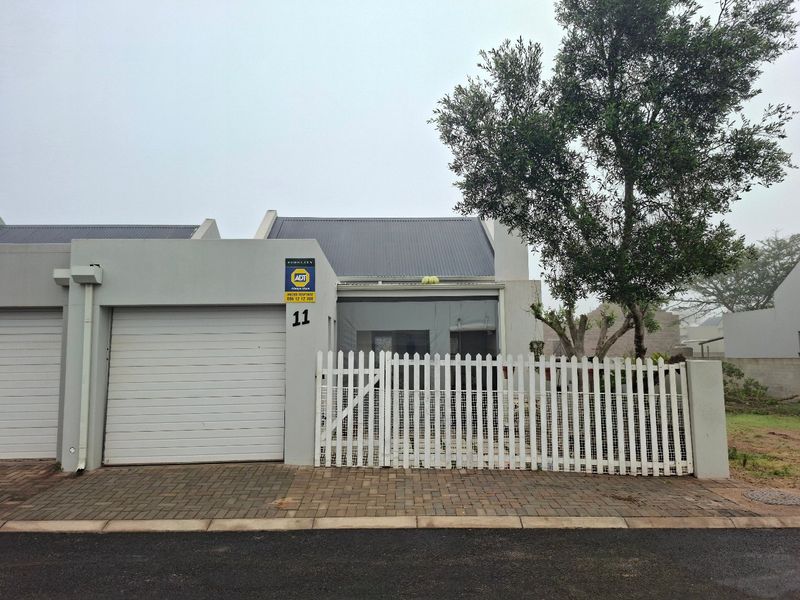 Front elevation of a residential property featuring a roller garage door, white picket fence, and paved driveway access.