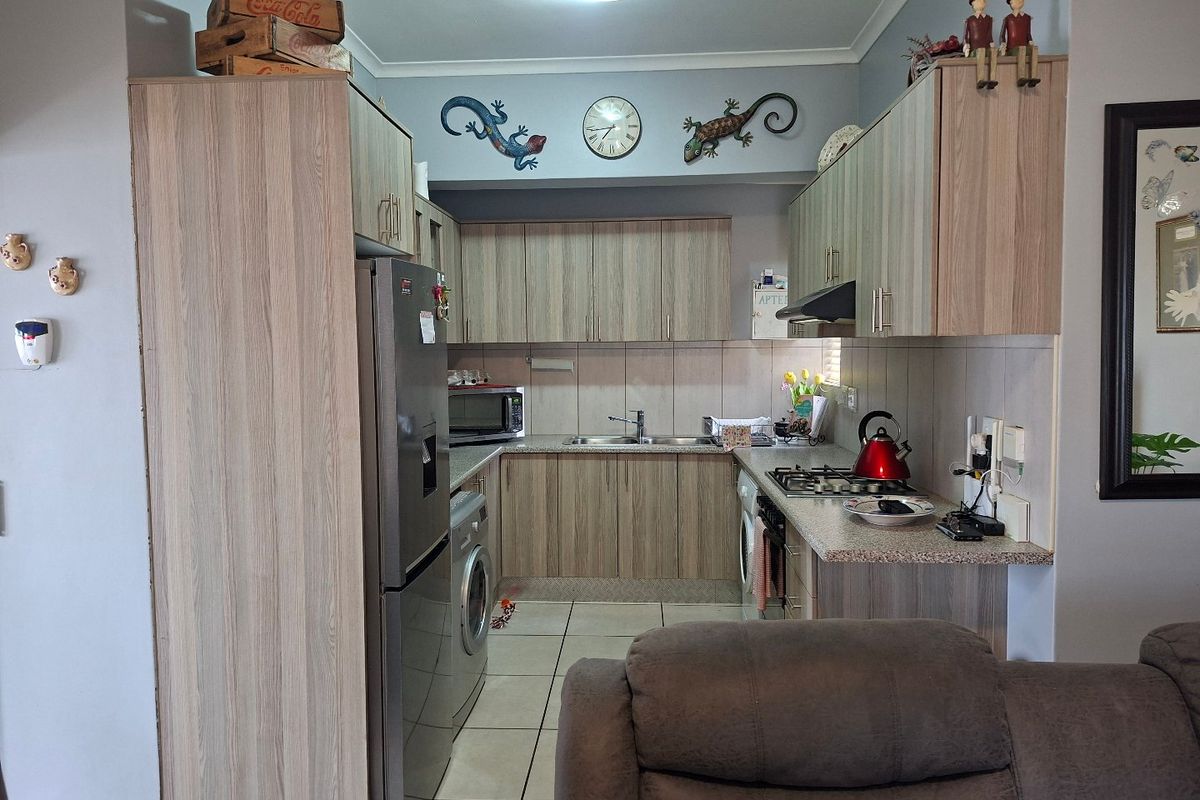 A functional kitchen featuring light wood-look cabinetry, stone-effect countertops, a gas hob, and integrated space for laundry appliances.