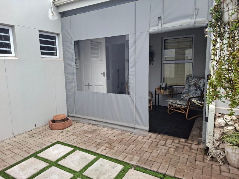 A covered patio area featuring paved flooring with artificial grass accents and a retractable outdoor blind for privacy and weather protection.