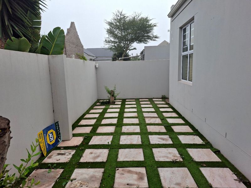 A private rear courtyard featuring a grid-pattern paved area with artificial grass infill, enclosed by high boundary walls.