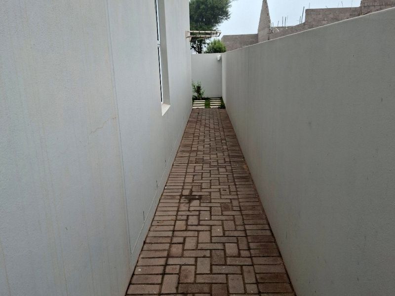A narrow paved side passage between the main building and a high boundary wall, providing access to the rear garden area.