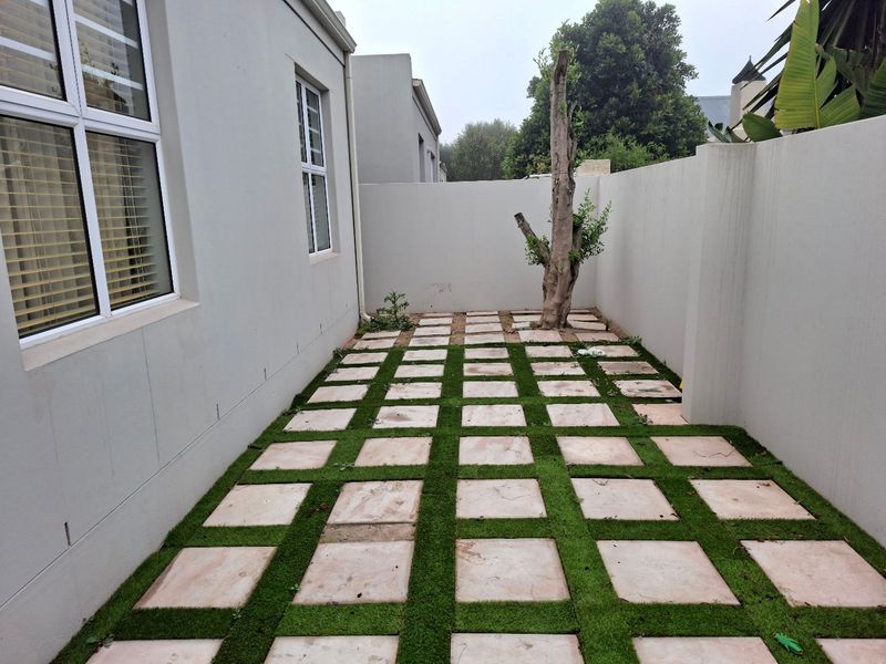A private rear courtyard featuring paved sections with grass infill, enclosed by high boundary walls.