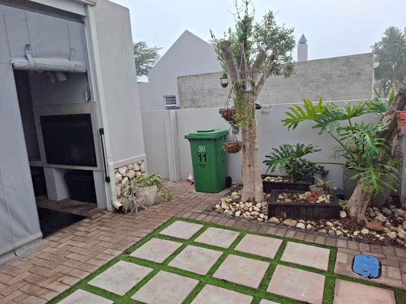 A paved outdoor patio area featuring a built-in braai, boundary walls, and landscaped garden elements.