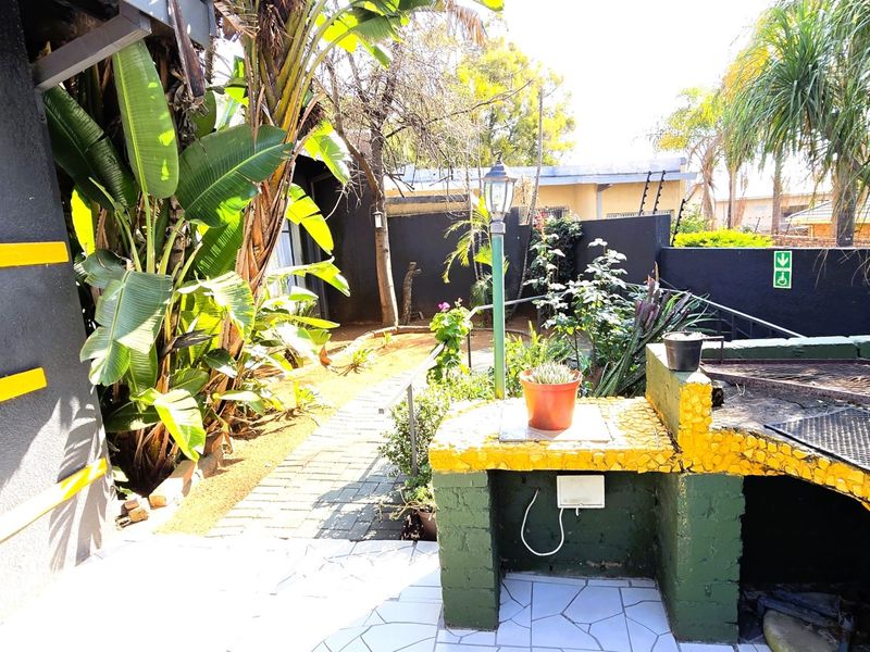 Outdoor patio area featuring a built-in braai, paved pathways, and established garden landscaping with boundary wall security.