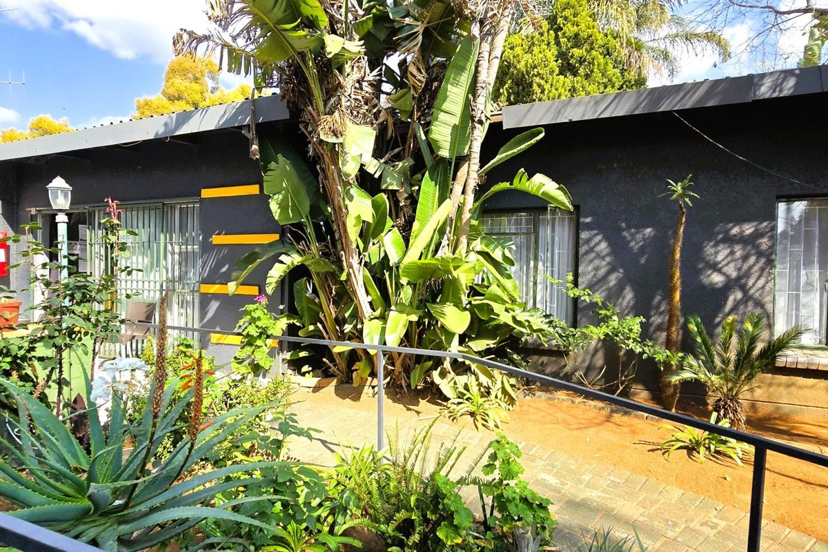 Rear exterior view of the property featuring a paved walkway, metal handrails, and established garden landscaping against the building facade.