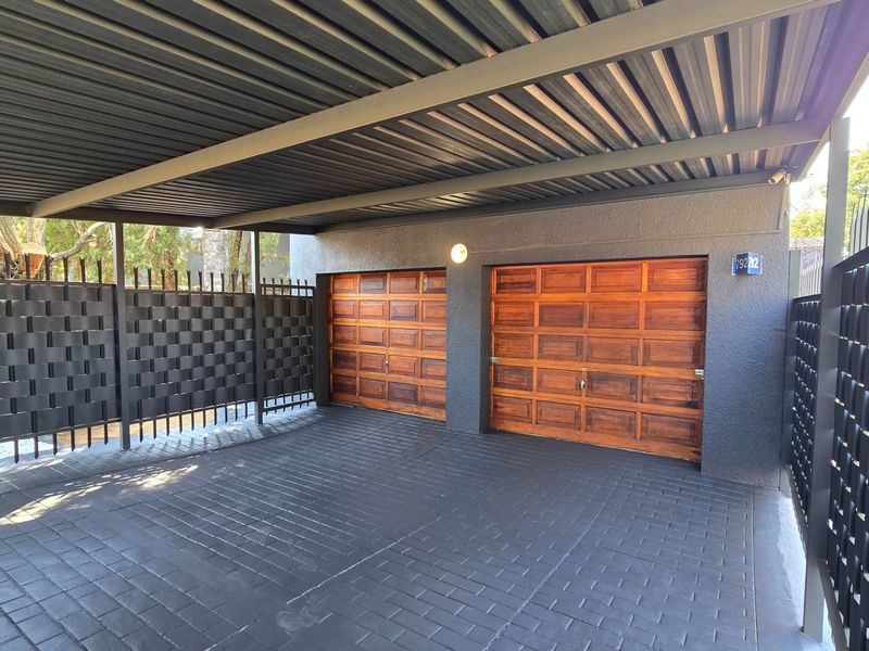 A well-maintained double garage featuring wooden doors, a covered carport area, and secure metal perimeter fencing.