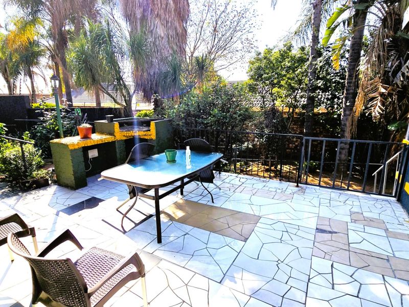 Outdoor patio area featuring a built-in braai, tiled flooring, and metal security railings, set within a garden environment.