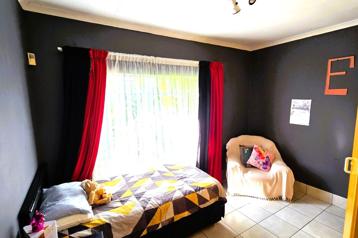 A bedroom featuring tiled flooring and a large window with curtain rails, providing natural light.