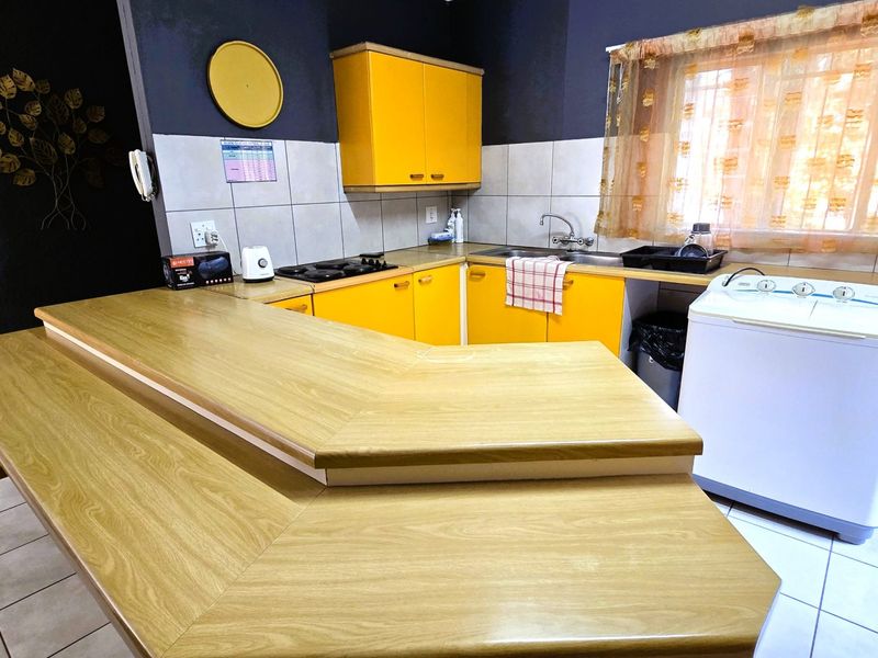 A functional kitchen featuring bright yellow cabinetry, a wood-look laminate breakfast bar, tiled backsplash, and a gas hob.
