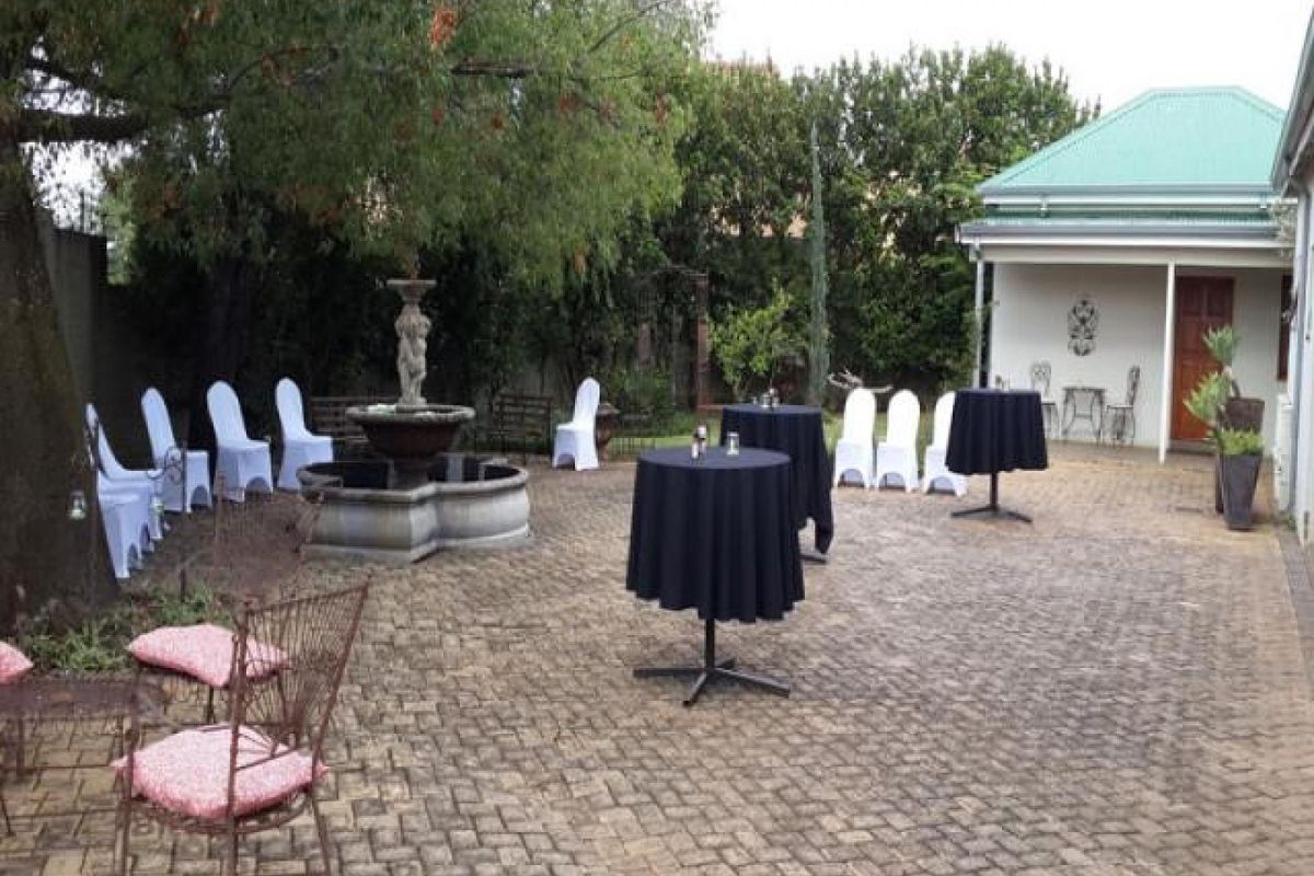 A spacious paved rear courtyard featuring a decorative stone fountain, mature trees, and a covered veranda area suitable for outdoor entertaining.