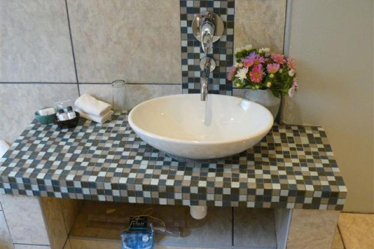 A bathroom vanity featuring a white vessel sink, wall-mounted chrome faucet, and a decorative mosaic tiled countertop.