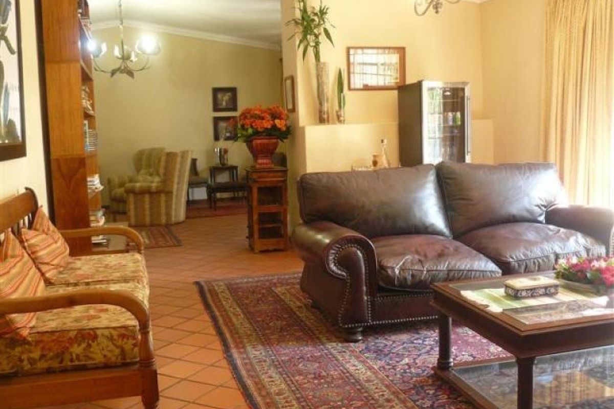 A spacious living room featuring terracotta floor tiles, an open-plan layout with an archway, and built-in shelving, offering a warm and traditional aesthetic.