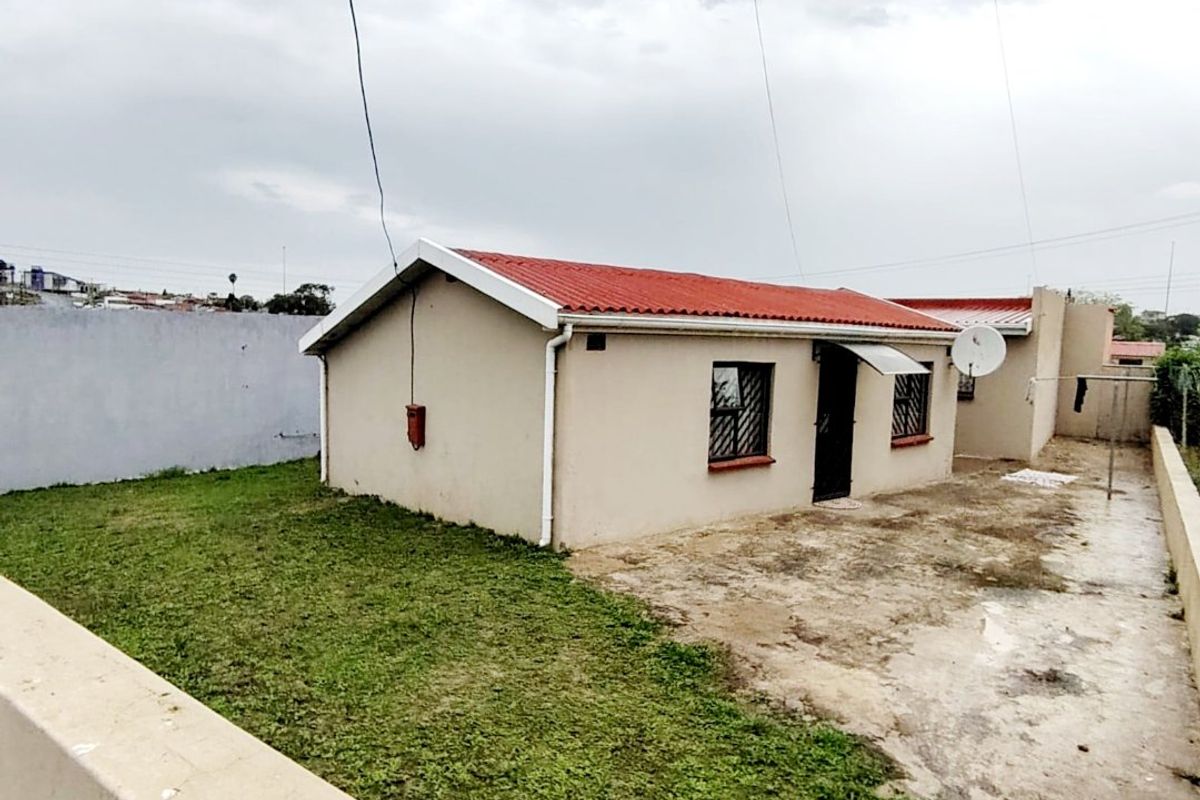 Rear view of a detached house featuring a concrete patio area, perimeter wall, and corrugated metal roof.