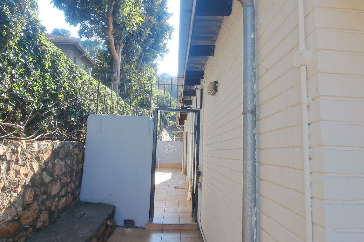 A side passage featuring a stone retaining wall, tiled flooring, and a metal security gate leading to the rear outdoor area.