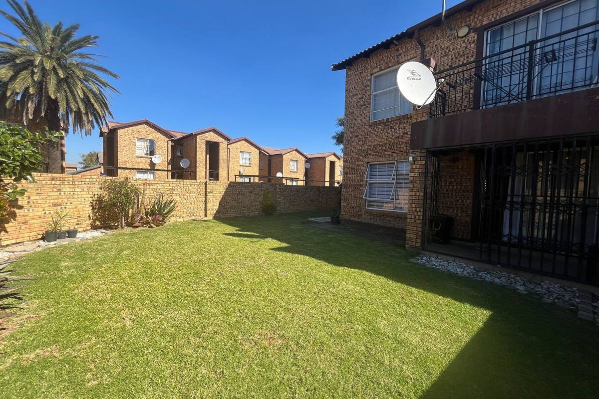 A private rear garden featuring a well-maintained lawn, face brick exterior, and a balcony with security gate access.