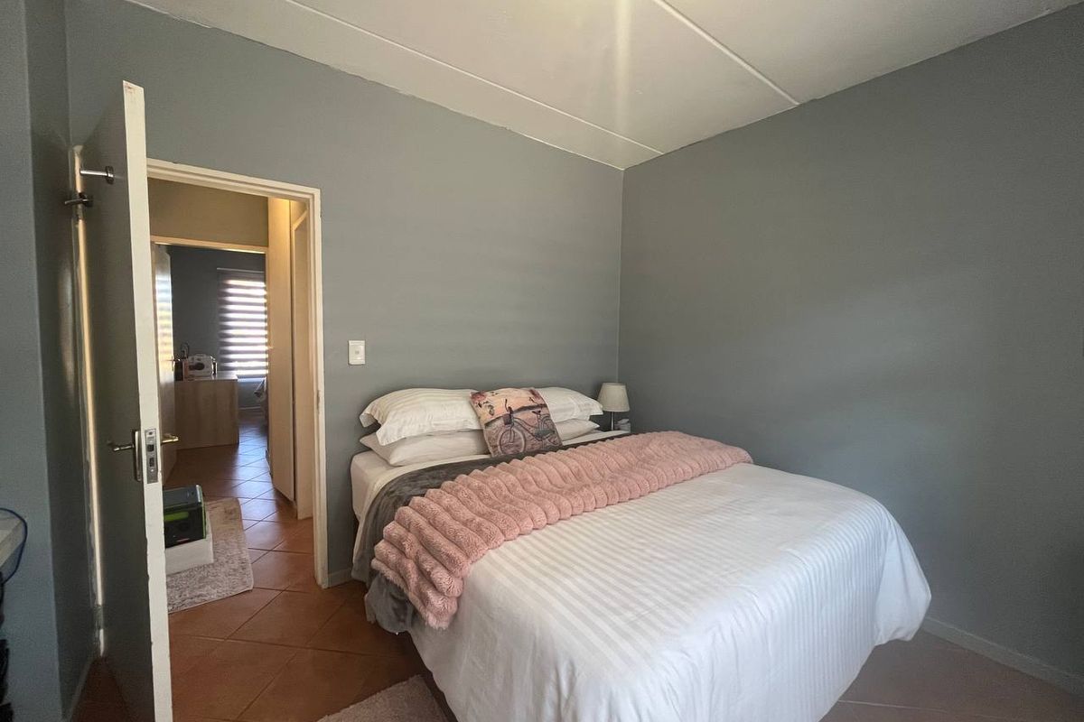 A bedroom featuring tiled flooring and neutral grey walls, with an open doorway leading to an adjacent room.
