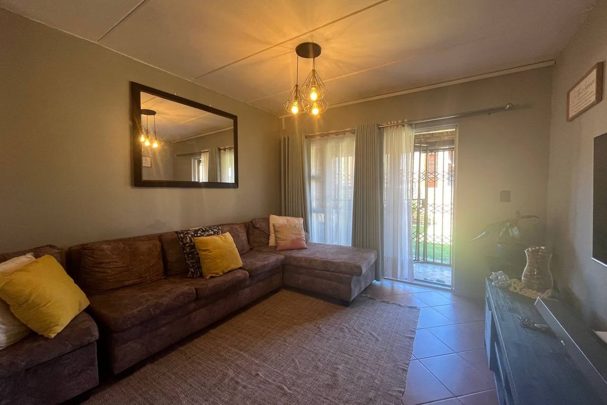 A comfortable living room featuring tiled flooring and a sliding glass door with security gate, providing direct access to the outdoor area.