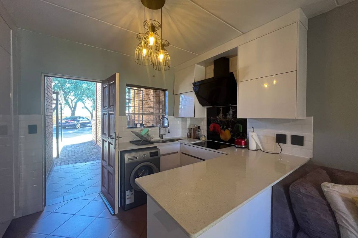 Compact kitchen featuring modern white cabinetry, stone countertops, integrated hob with extractor, and a tiled backsplash, with direct access to the exterior.