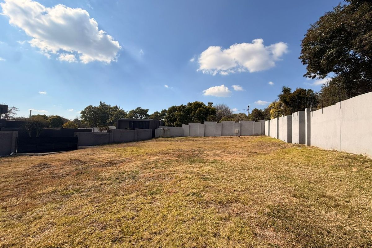 A vacant residential plot featuring a level grassed area enclosed by perimeter concrete walls.