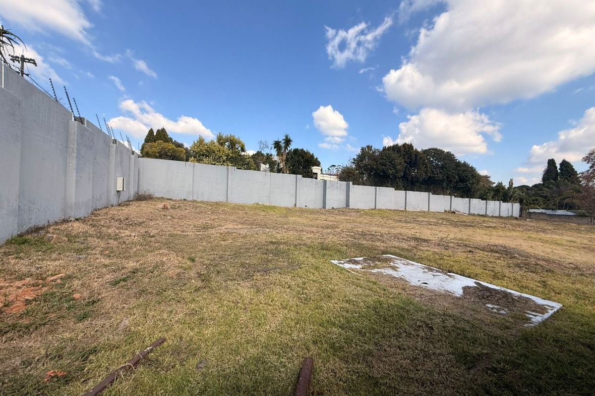A vacant residential plot featuring a perimeter wall with installed electric fencing, offering a clear space for future development.