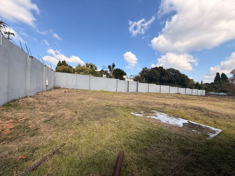 A vacant residential plot featuring a perimeter wall with installed electric fencing, offering a clear space for future development.