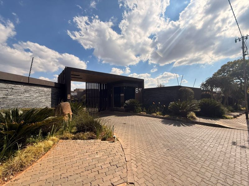 A modern residential entrance featuring a paved driveway, stone-clad boundary walls, electric fencing, and a secure gated access point.