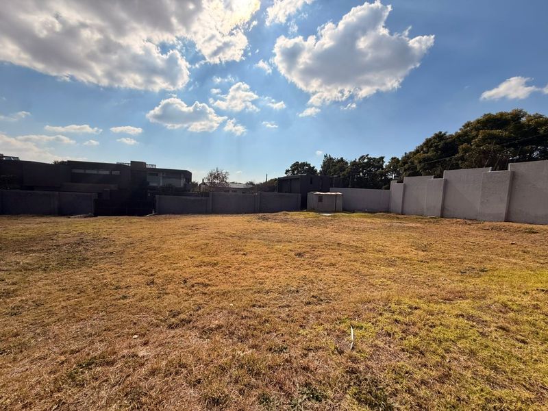 A vacant residential plot featuring a level grass lawn enclosed by perimeter boundary walls.